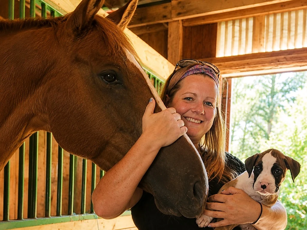 Carolyn in stable stall demonstrating multi-species desensitization with horse and calm puppy